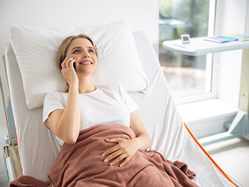Eine Frau in einem Krankenhausbett telefoniert auf ihrem Mobiltelefon.